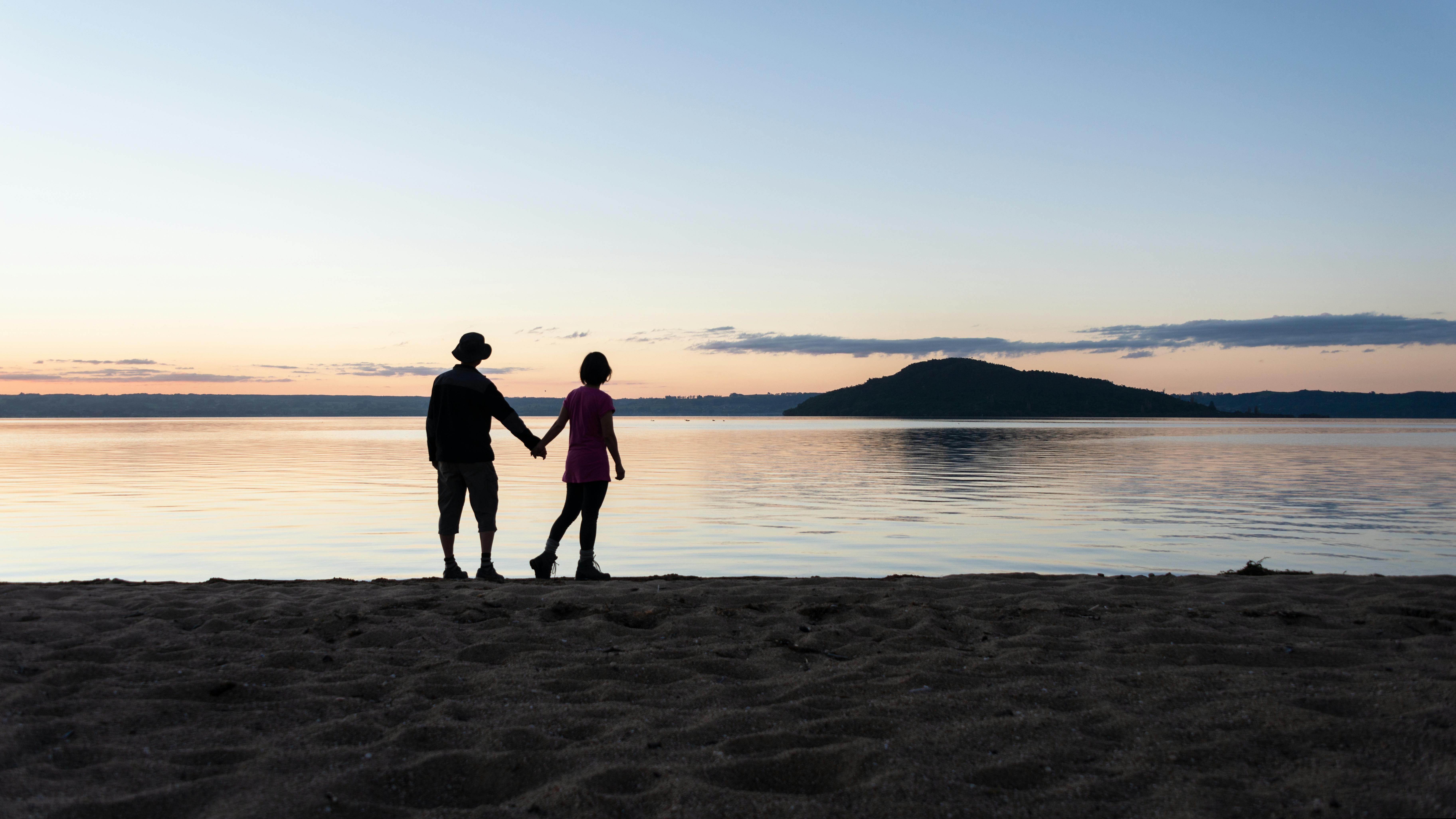 a man and a woman holding hands looking reflectively out at the water