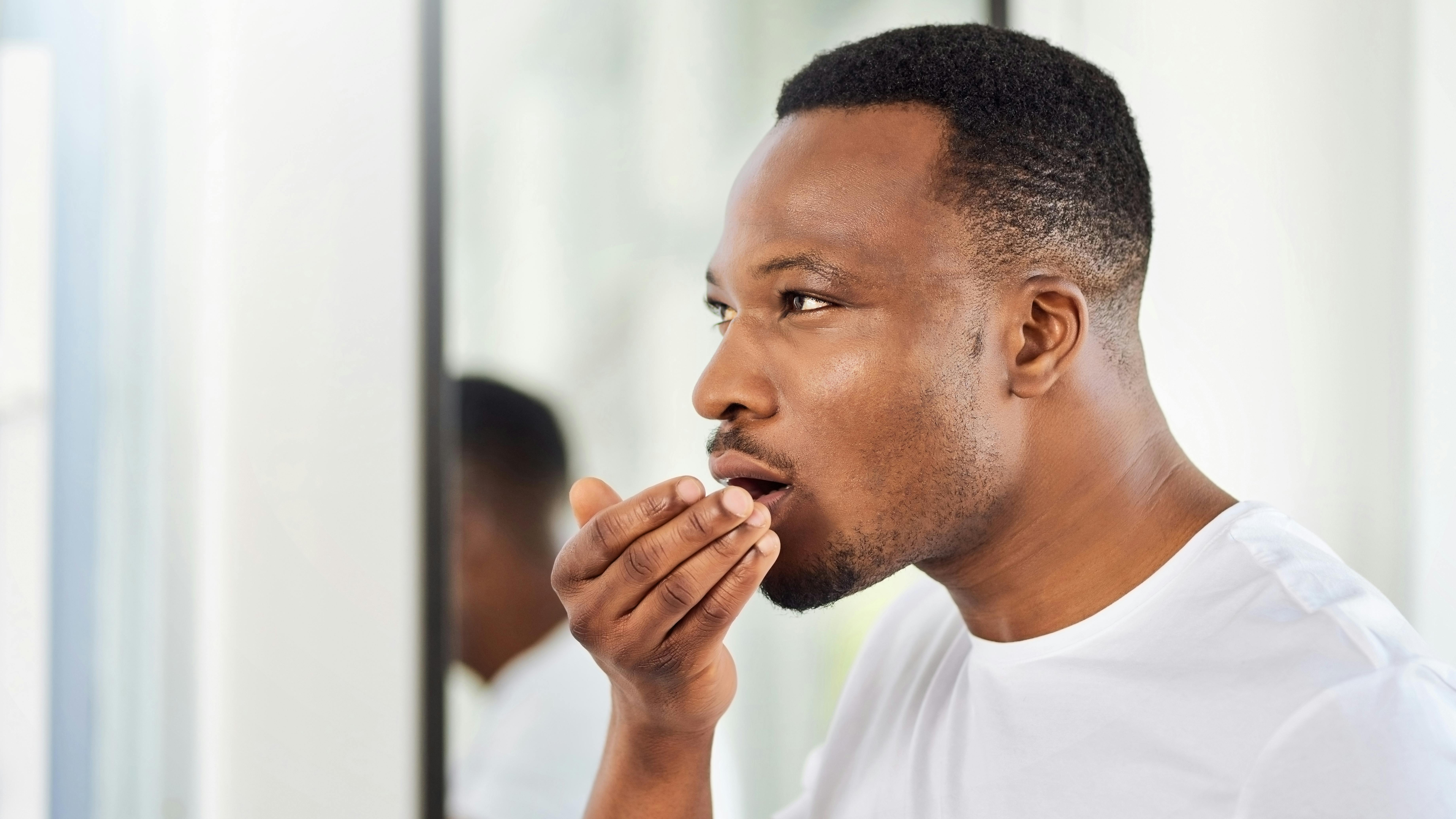 a man with a hand in front of his mouth smelling his breath