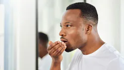 a man with a hand in front of his mouth smelling his breath a man with a hand in front of his mouth smelling his breath